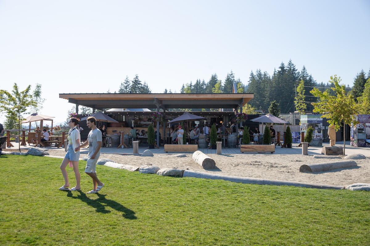 People enjoying an outdoor café with patio seating and umbrellas at a park